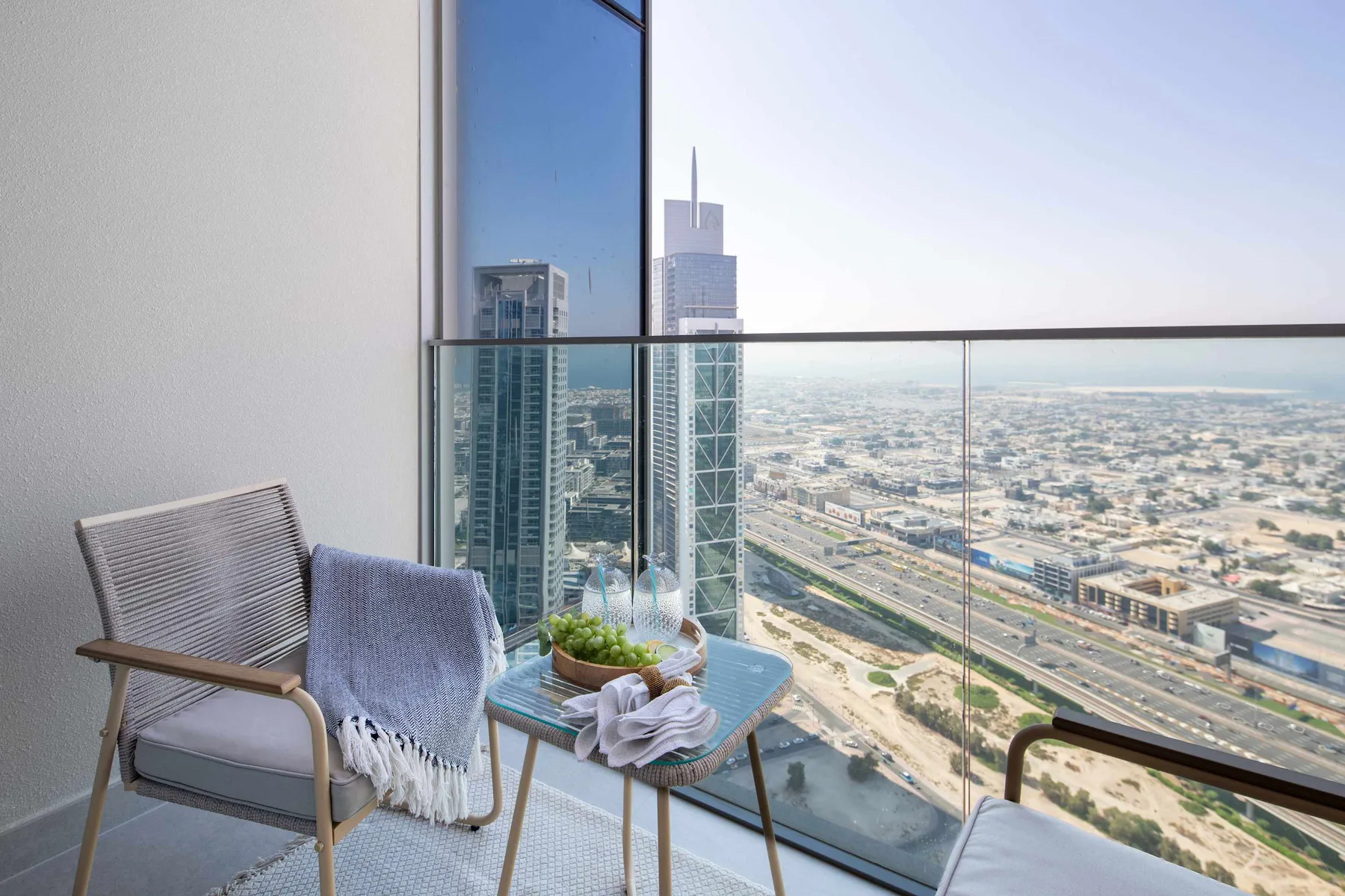 A balcony seating area overlooks a city through a glass railing.