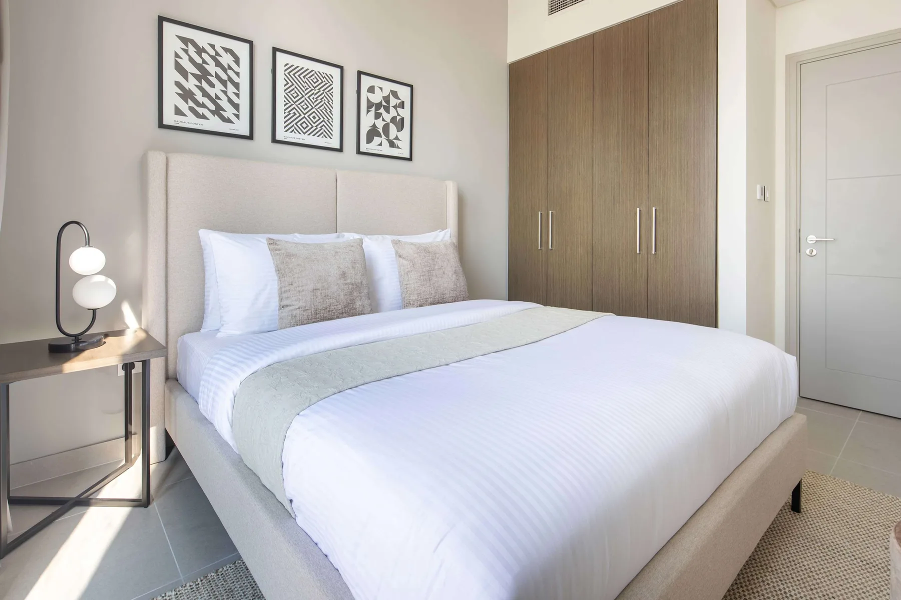 A bright bedroom with a neatly made bed and a large wooden wardrobe.