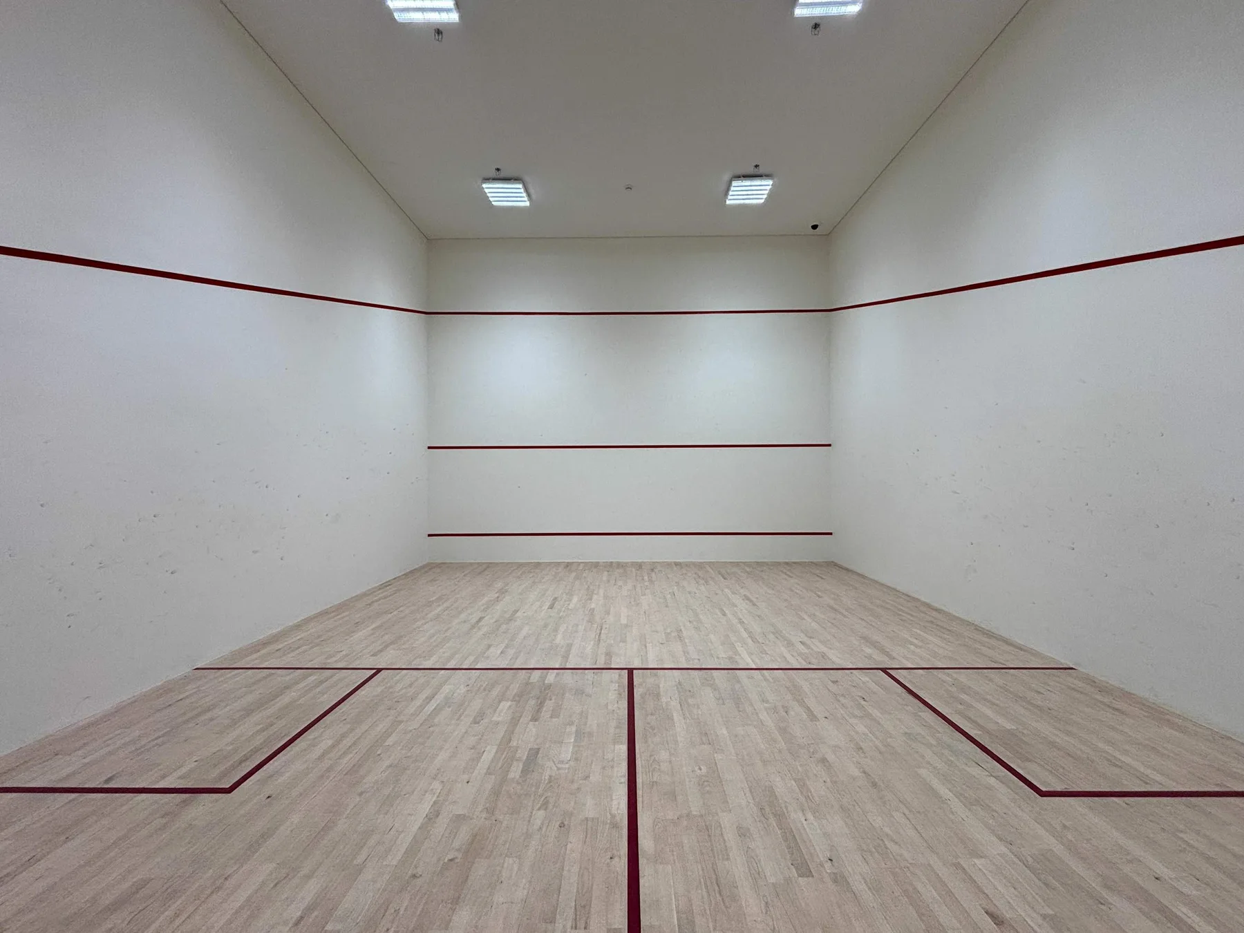 An indoor squash court with painted boundary lines and overhead lights.