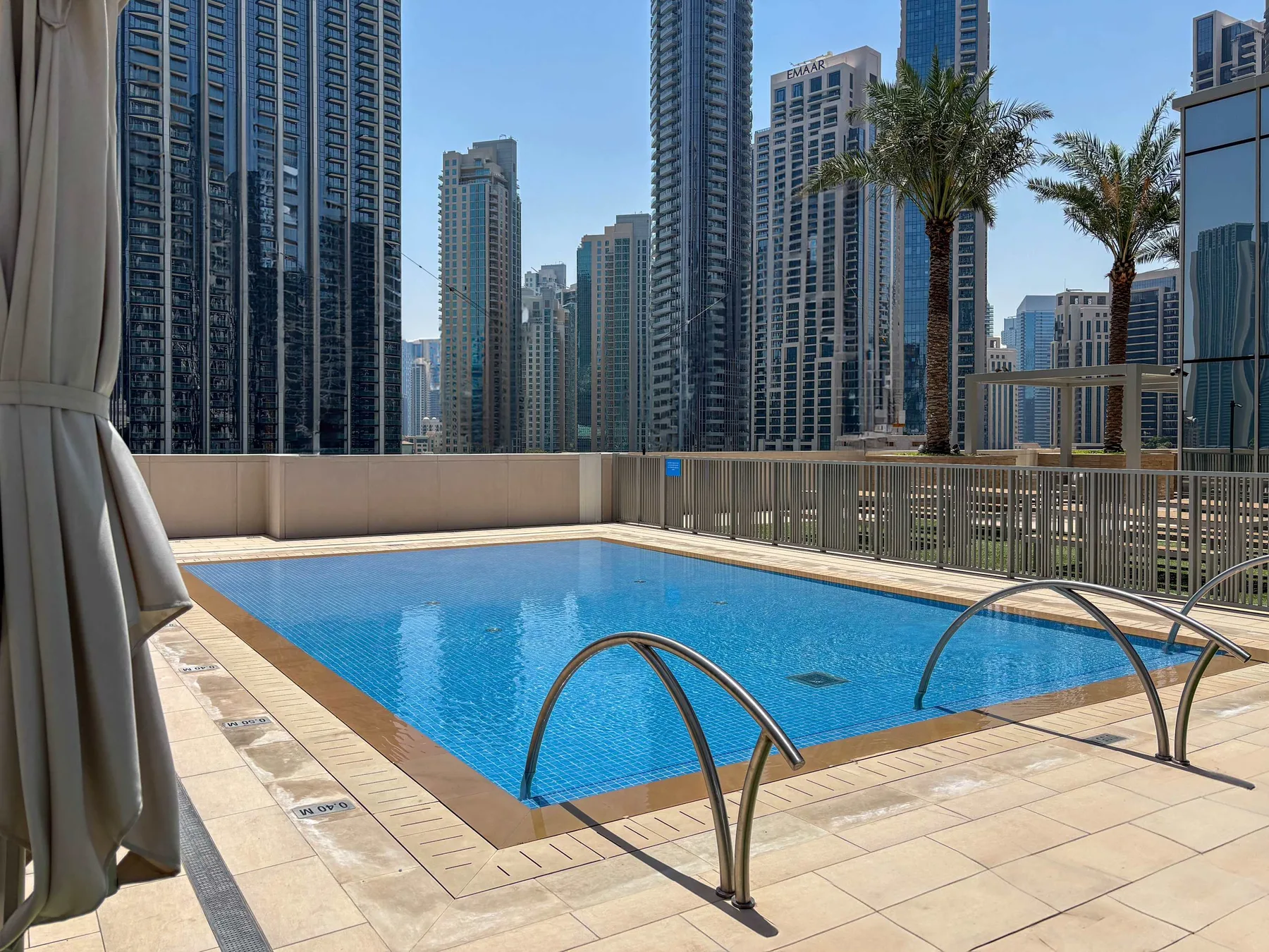 A rooftop swimming pool sits beside a railing, with high-rise buildings in the background.
