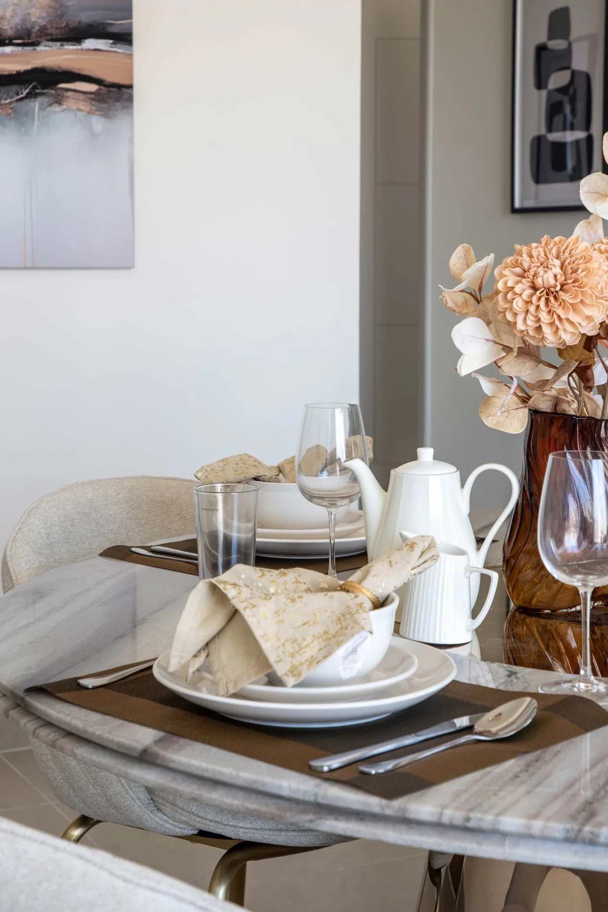 A dining table is set with plates, glassware, and a white teapot.