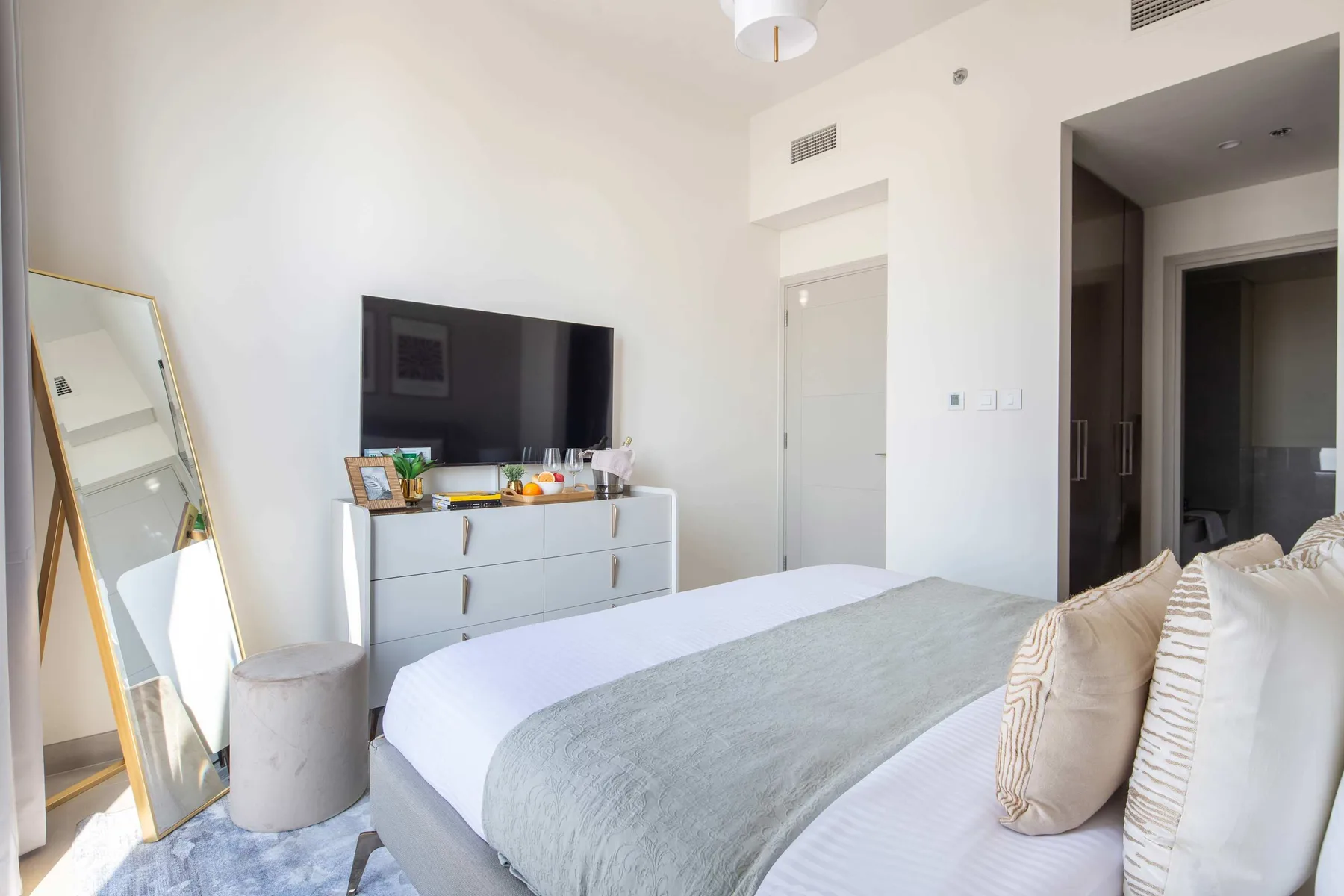 A bright bedroom with a neatly made bed and a television on a dresser.