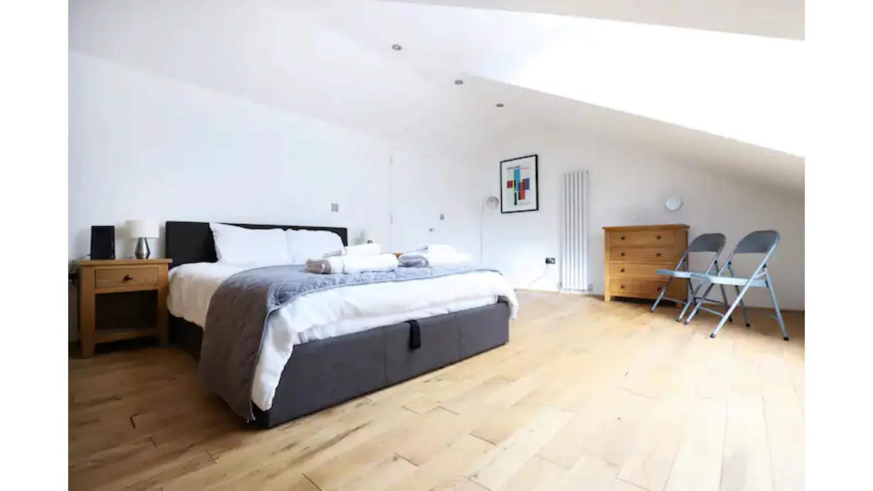 A bedroom with a bed, a wooden dresser, and two folding chairs.