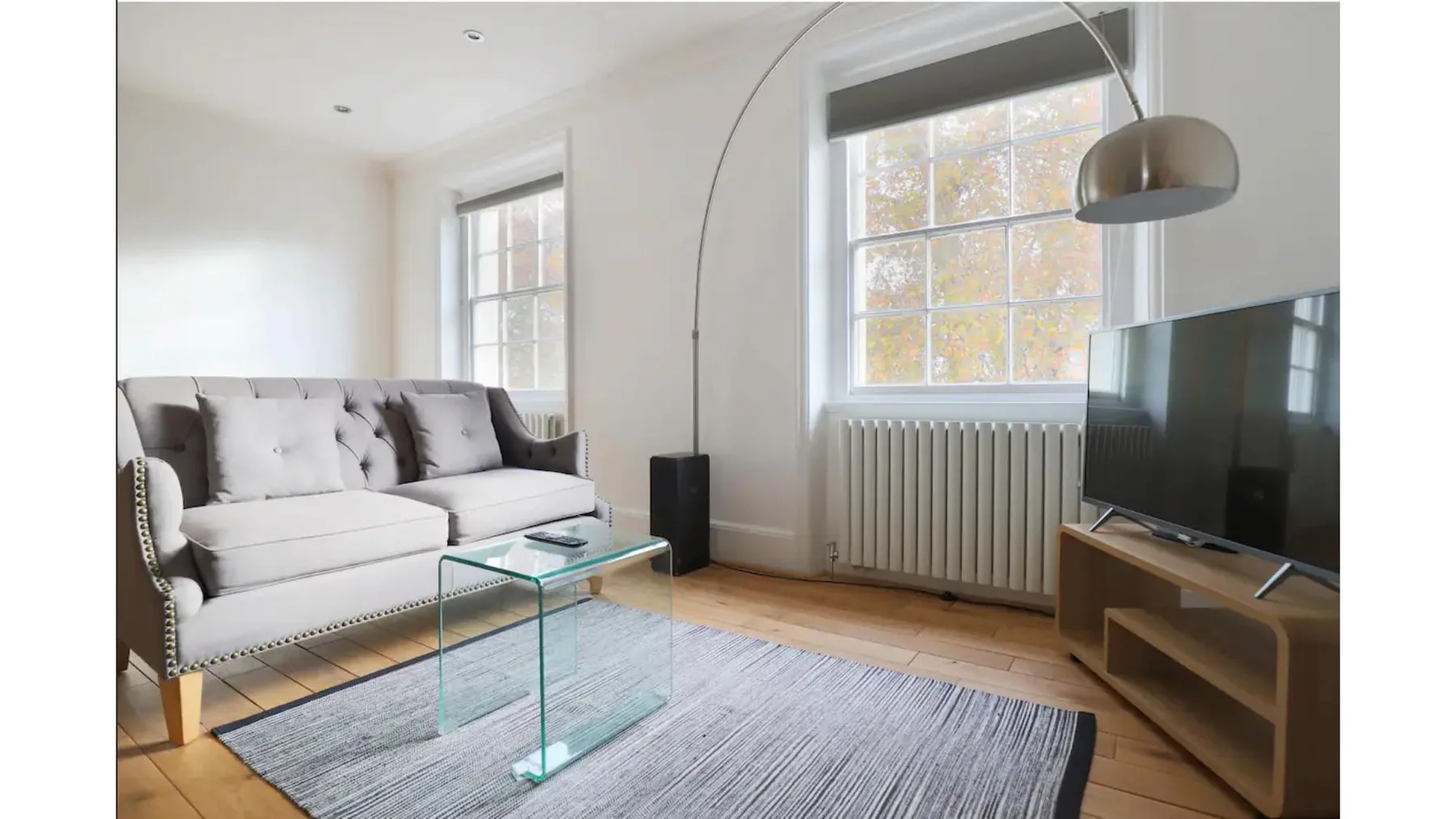 A bright living room with a sofa, glass coffee table, and television.