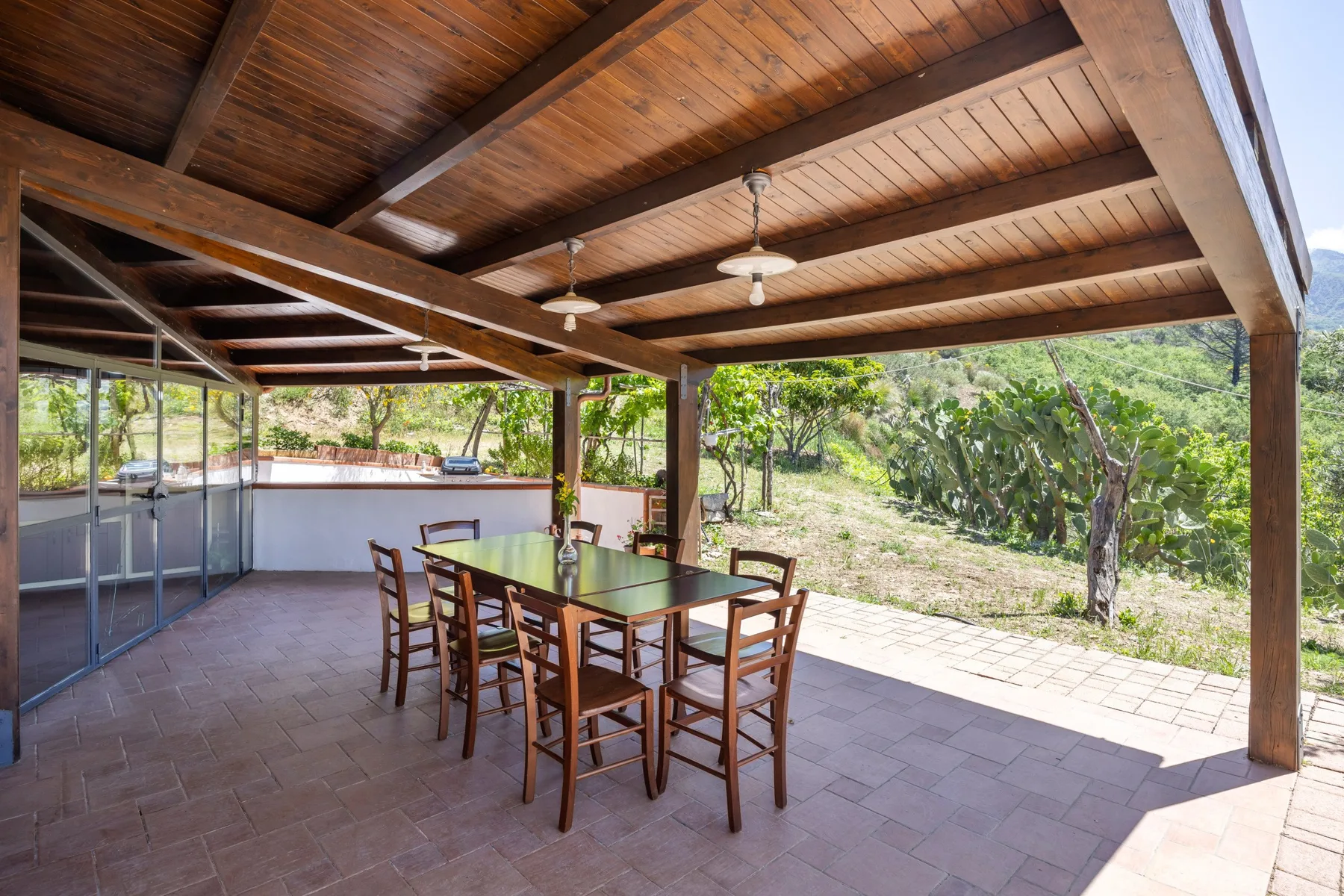 Un comedor exterior cubierto con una mesa y sillas de madera da a un jardín verde.
