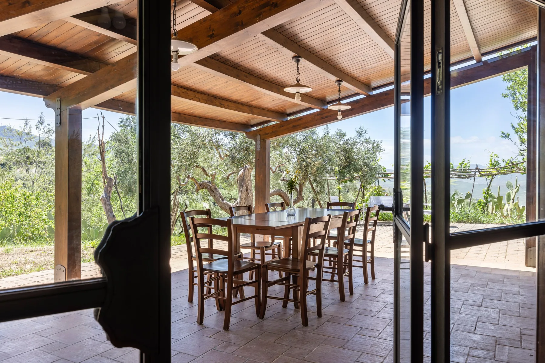 Una zona de comedor al aire libre cubierta, con mesa y sillas de madera, da a la vegetación.