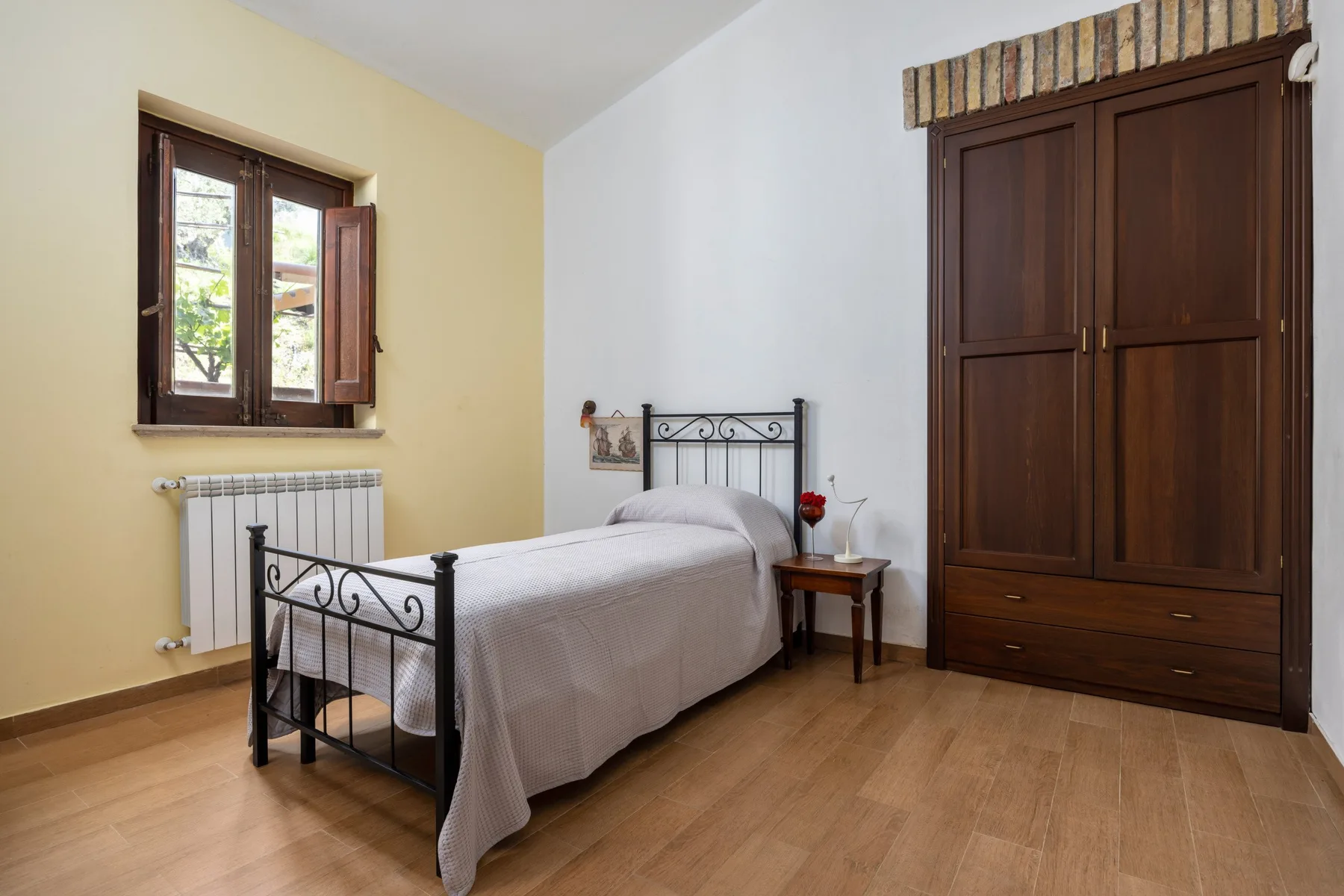 Un dormitorio con una cama de metal, un armario de madera y una ventana.