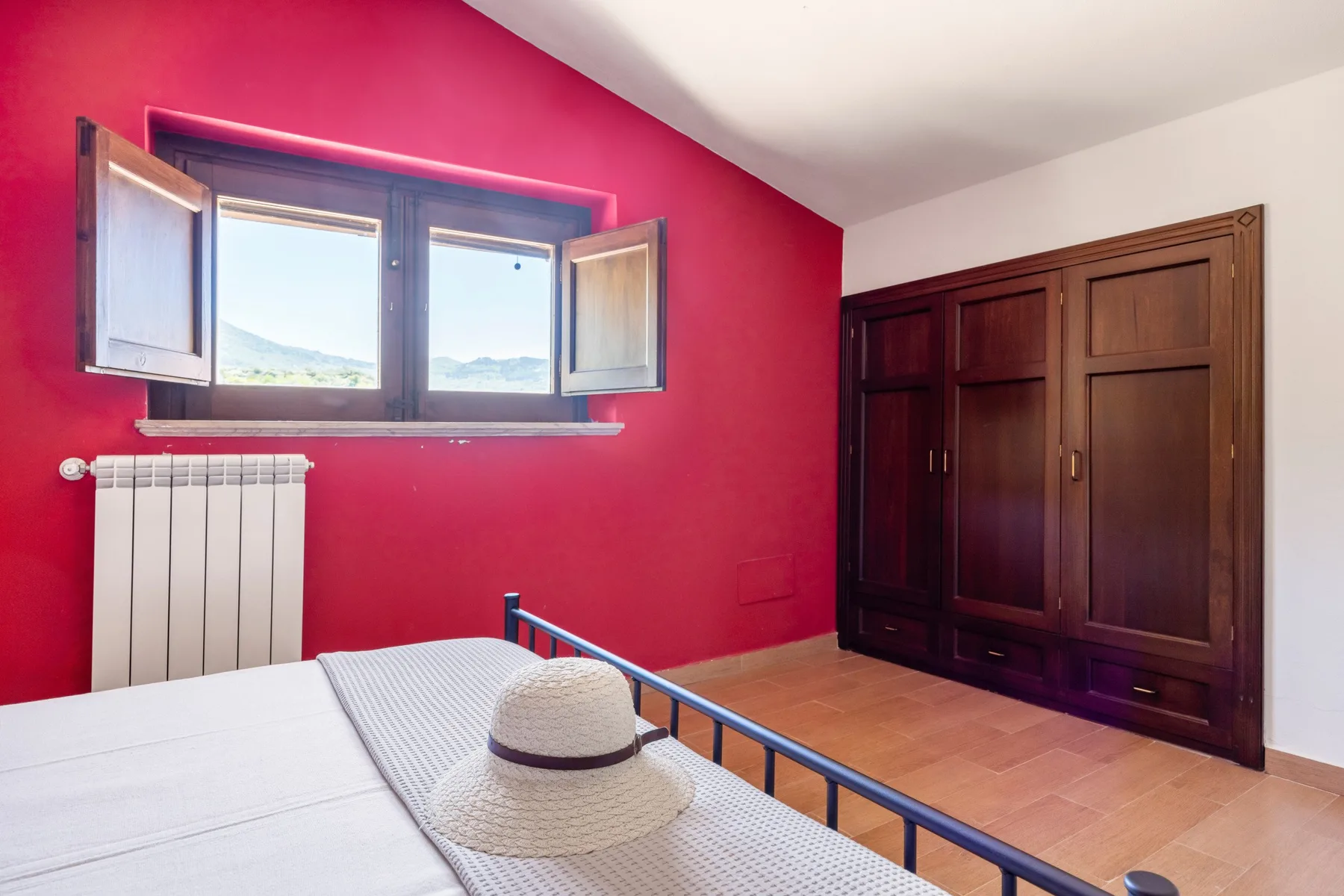 Un dormitorio con una cama, una pared roja y un armario grande de madera.
