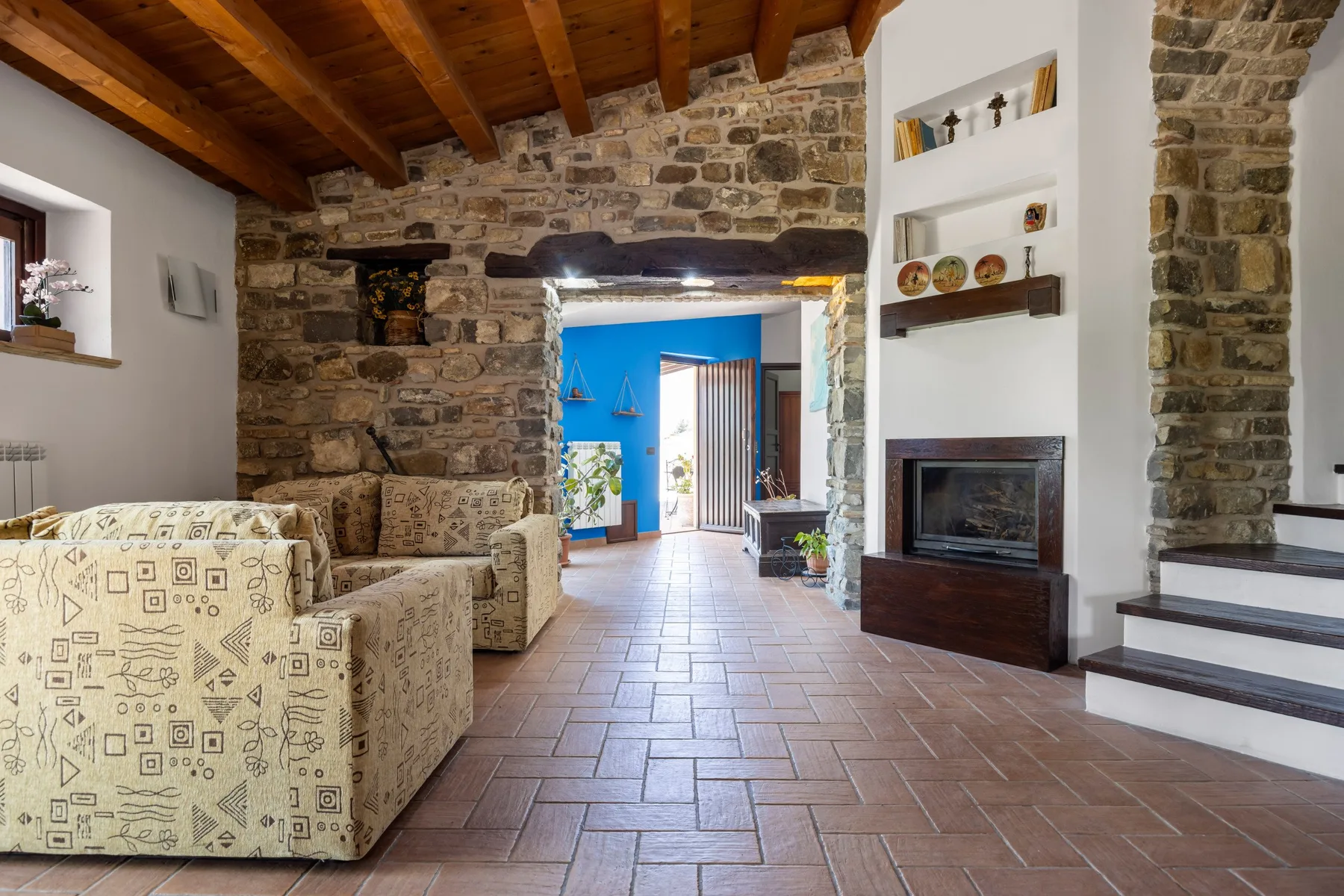 Una sala de estar de piedra con asientos estampados, chimenea y suelo de baldosas.