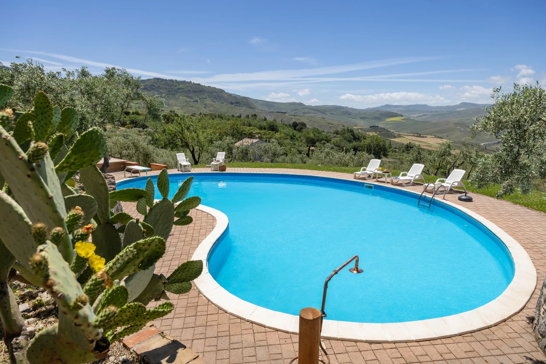 Una piscina con asientos reclinables da a un paisaje de colinas verdes.