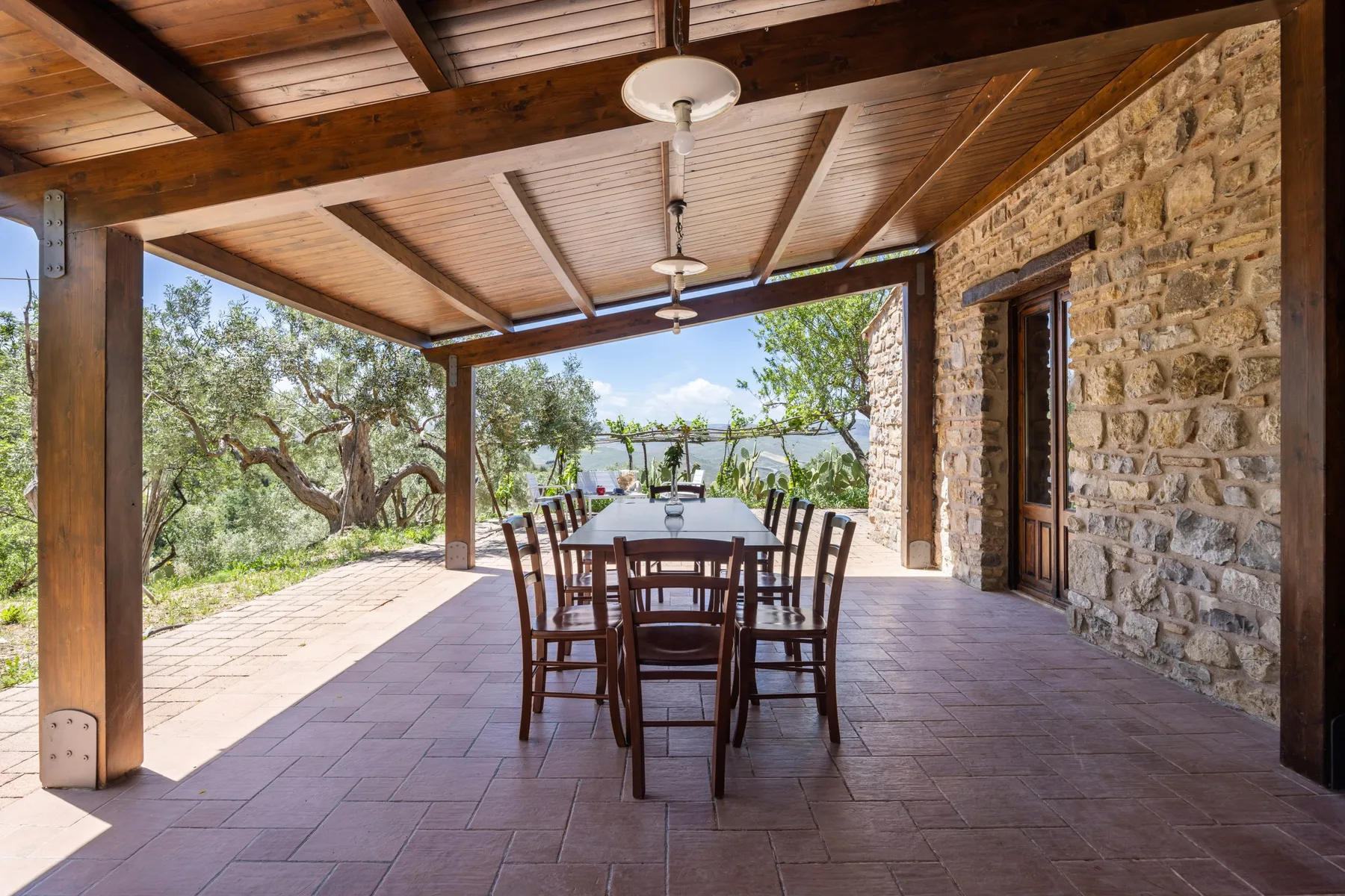 Comedor exterior cubierto con una mesa larga bajo vigas de madera expuestas.