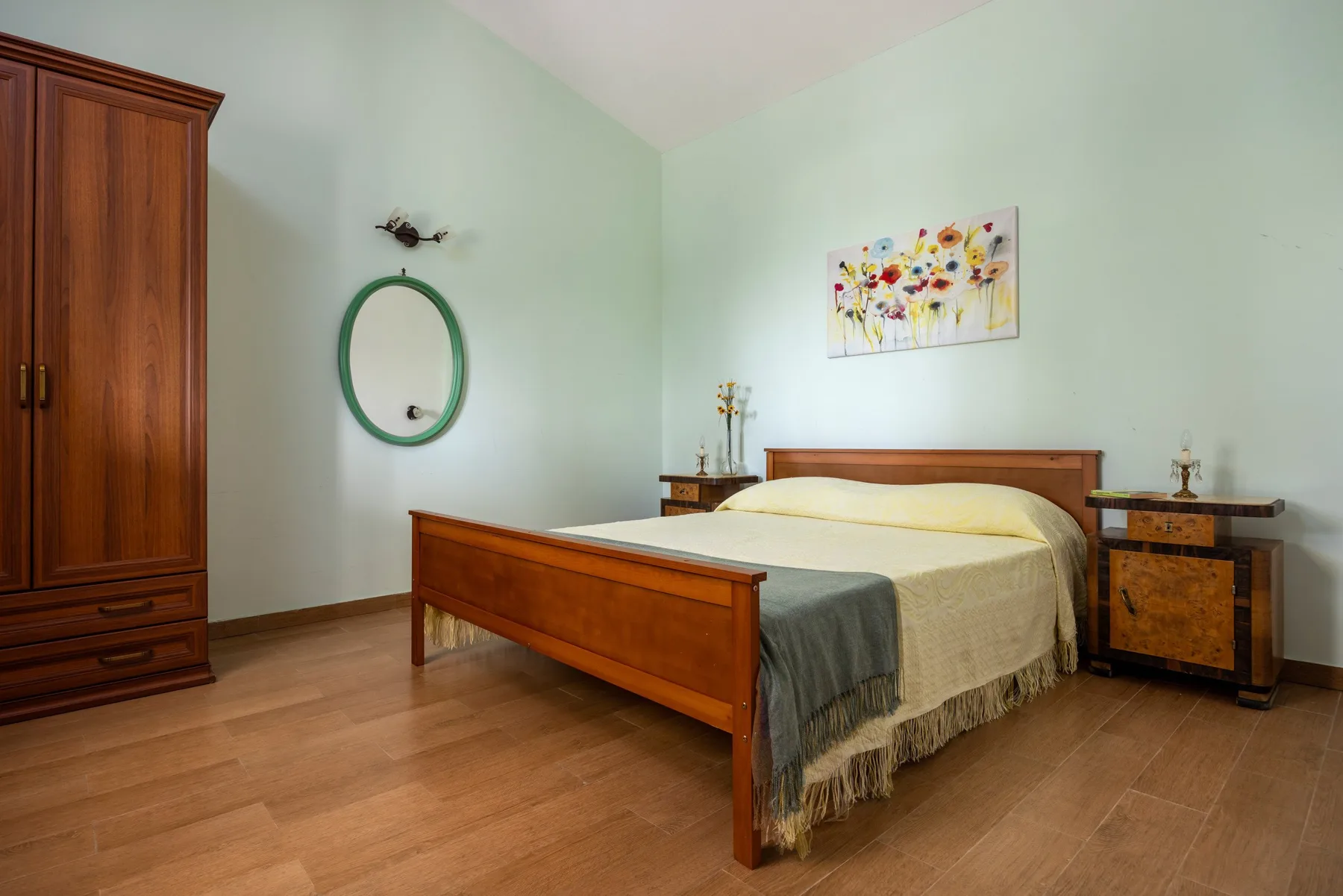 Un dormitorio con una cama de madera, mesitas de noche y un cuadro floral.