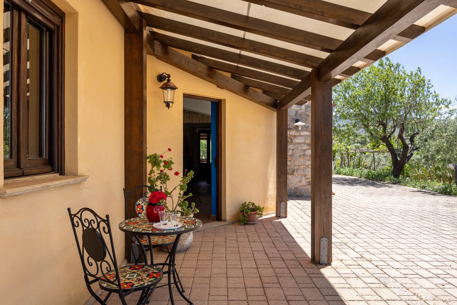 Un patio exterior cubierto con una mesa pequeña y sillas junto a una zona pavimentada soleada.