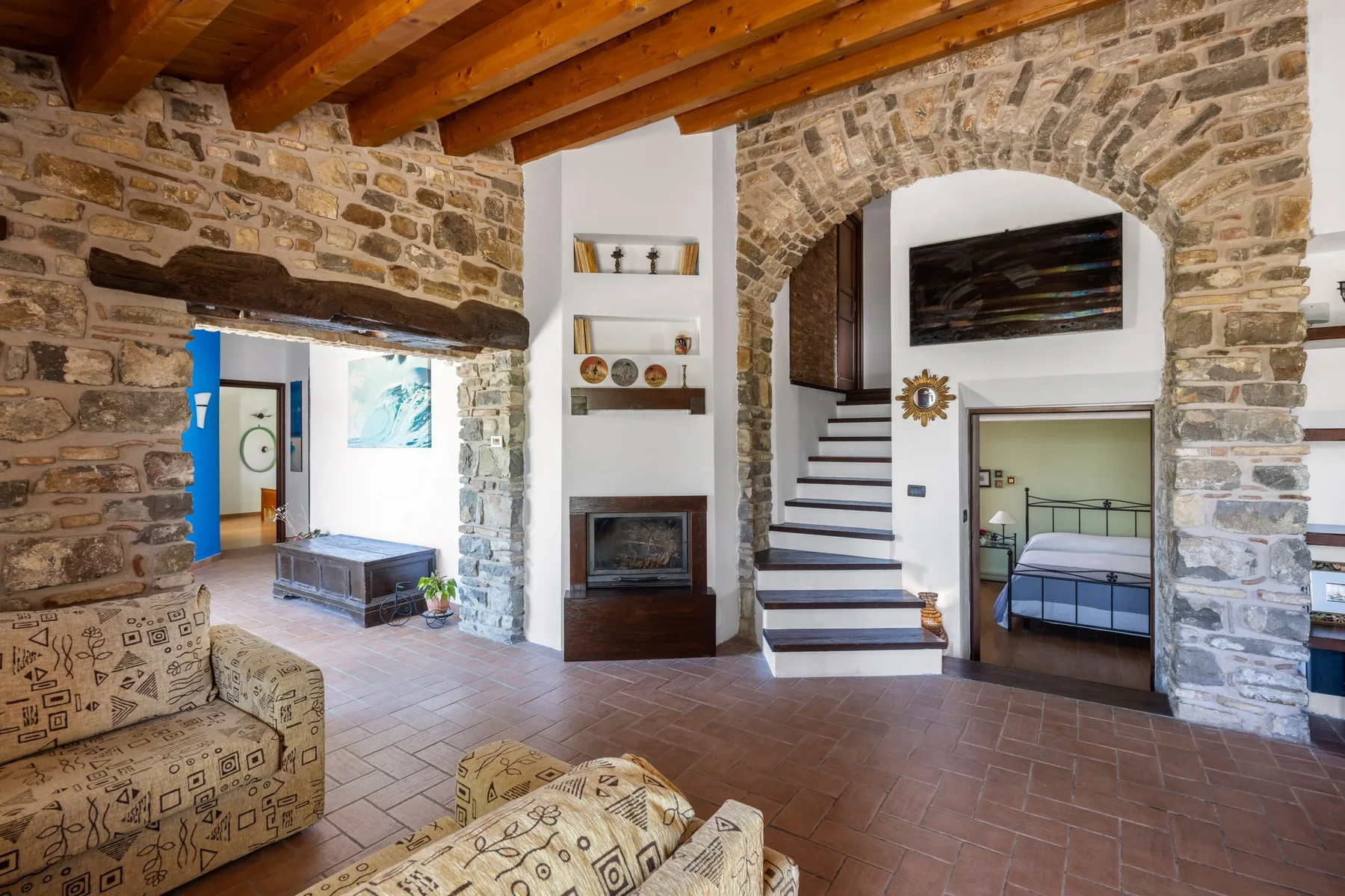 Un interior de piedra con una escalera, una chimenea y asientos bajo vigas de madera expuestas.