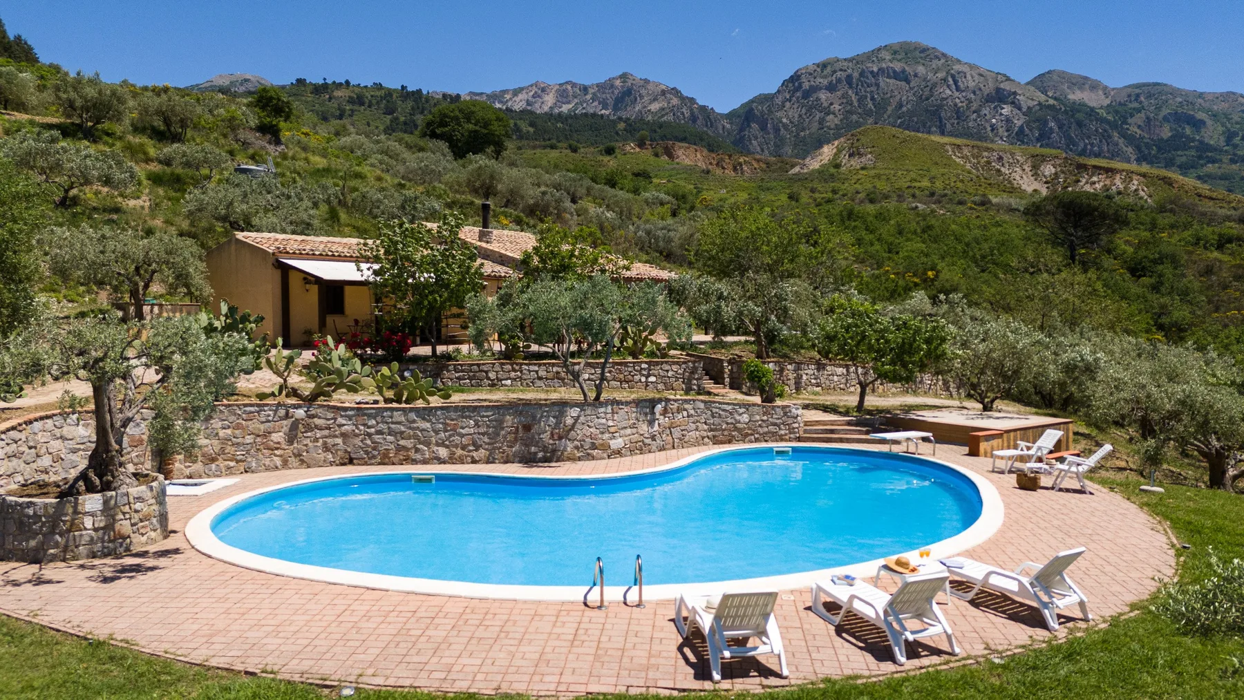 Una piscina y un patio rodeados de jardines, con montañas a lo lejos.