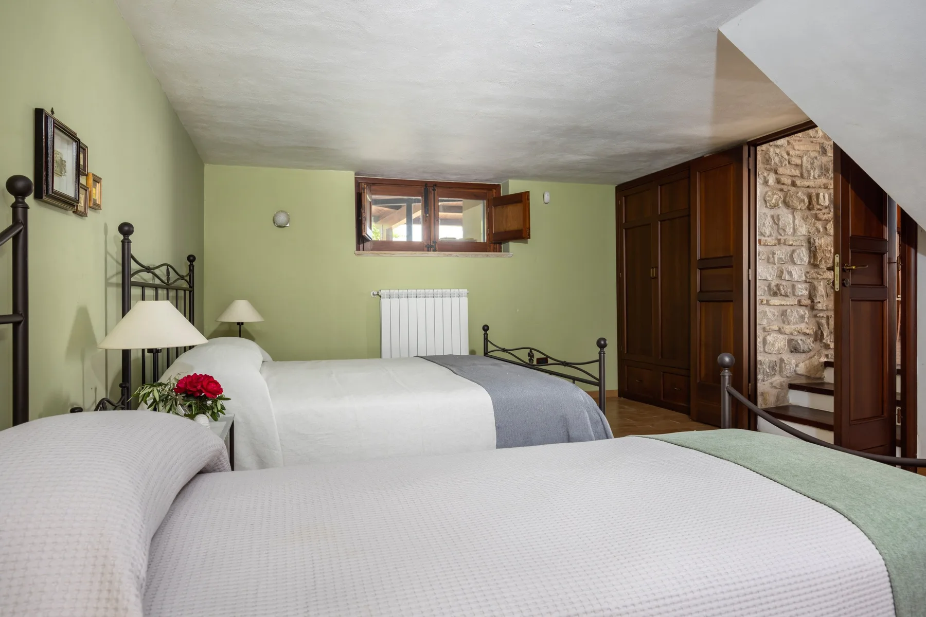 Un dormitorio con dos camas, paredes verde claro y una ventana pequeña.