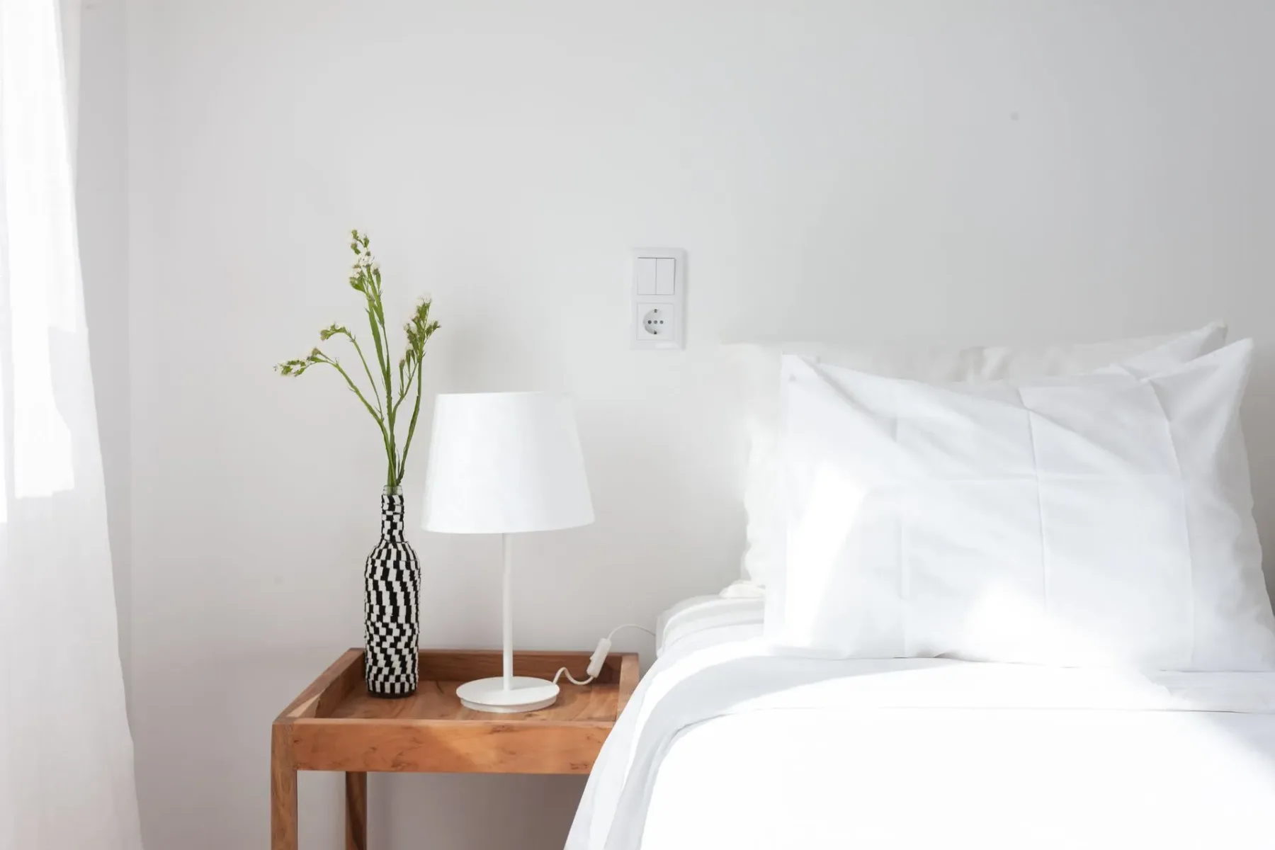 Dormitorio con una cama, mesa de noche, lámpara y florero con flores