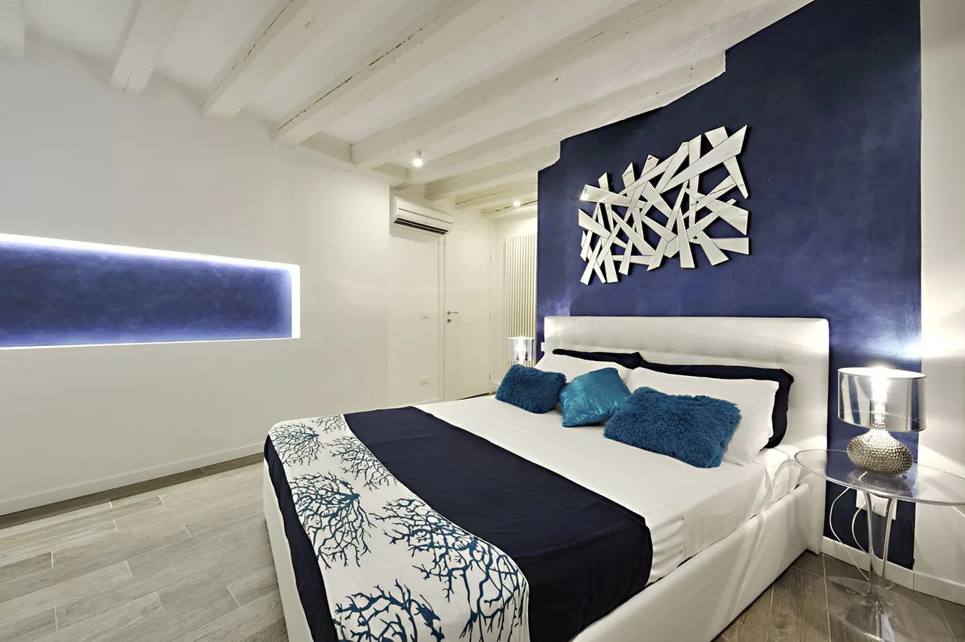 A bedroom with a white bed, blue accent wall, and decorative wall art.