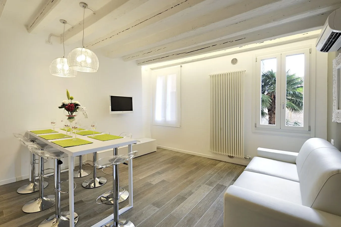 A bright dining and living area with a table, white seating, and large windows.