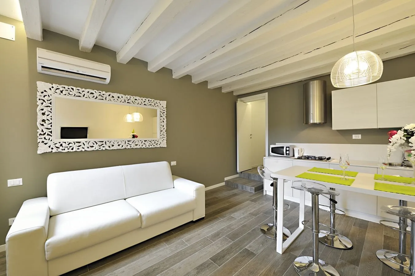 A bright open-plan living area and kitchen with white seating and a dining counter.