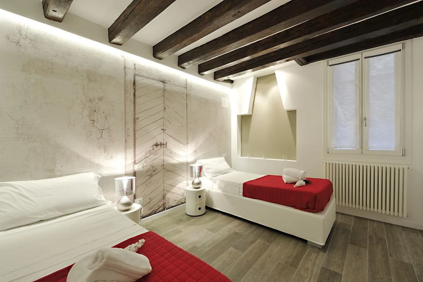 A bedroom with two beds, red bedspreads, and exposed ceiling beams.