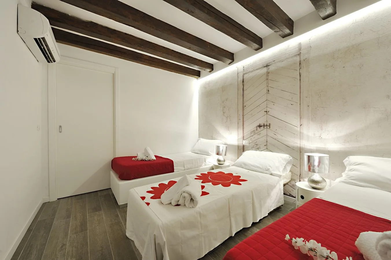 A bedroom with white beds, red bedspreads, and dark exposed ceiling beams.
