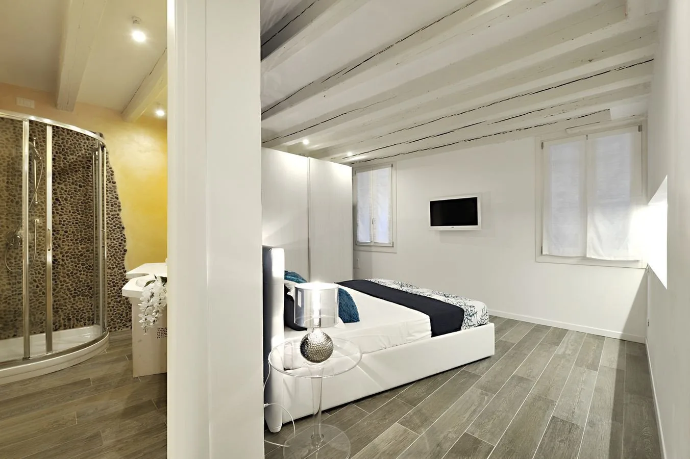 A bedroom with a bed, a wall-mounted television, and windows.