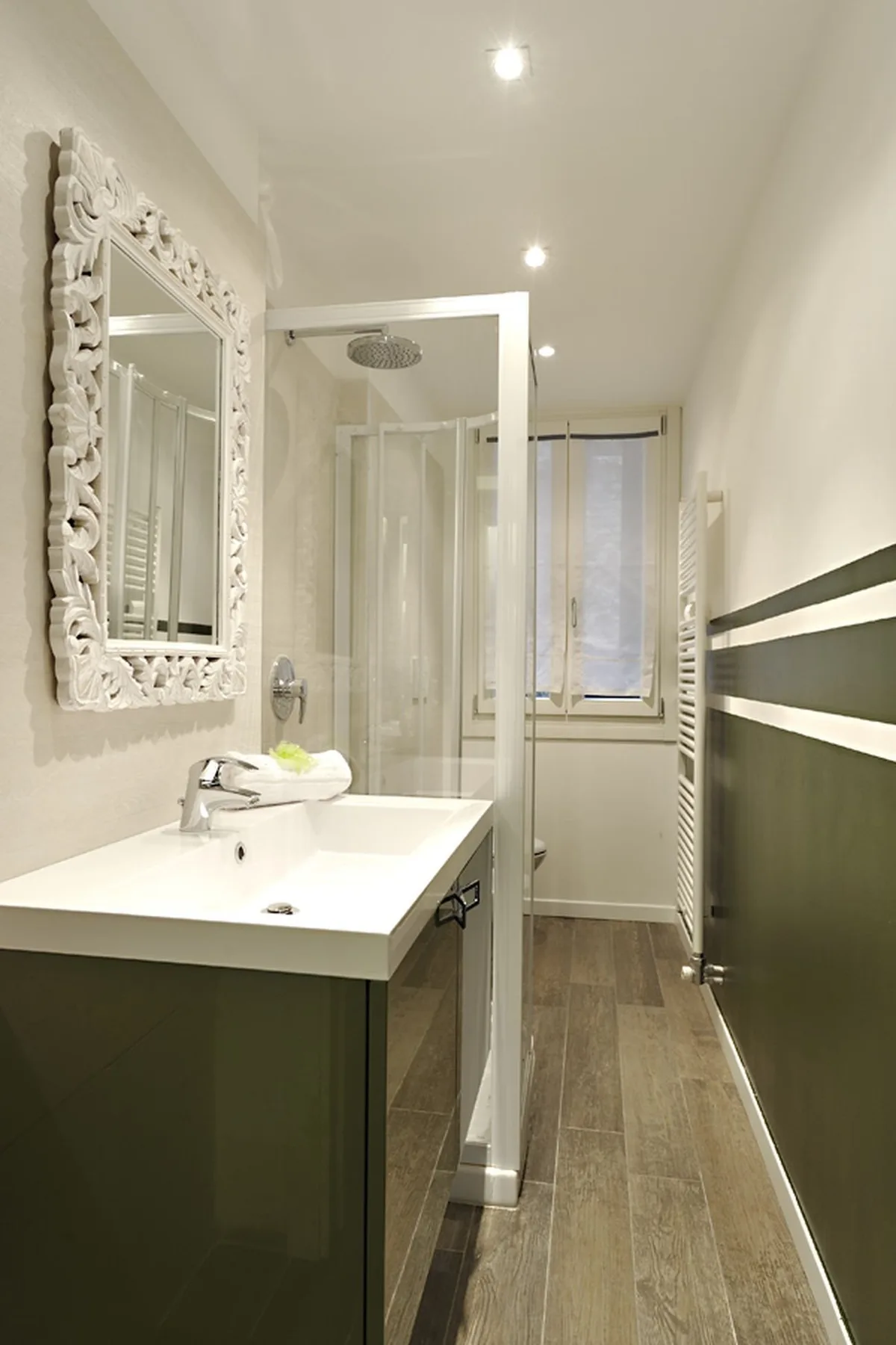 A narrow bathroom with a sink, ornate mirror, and glass shower.