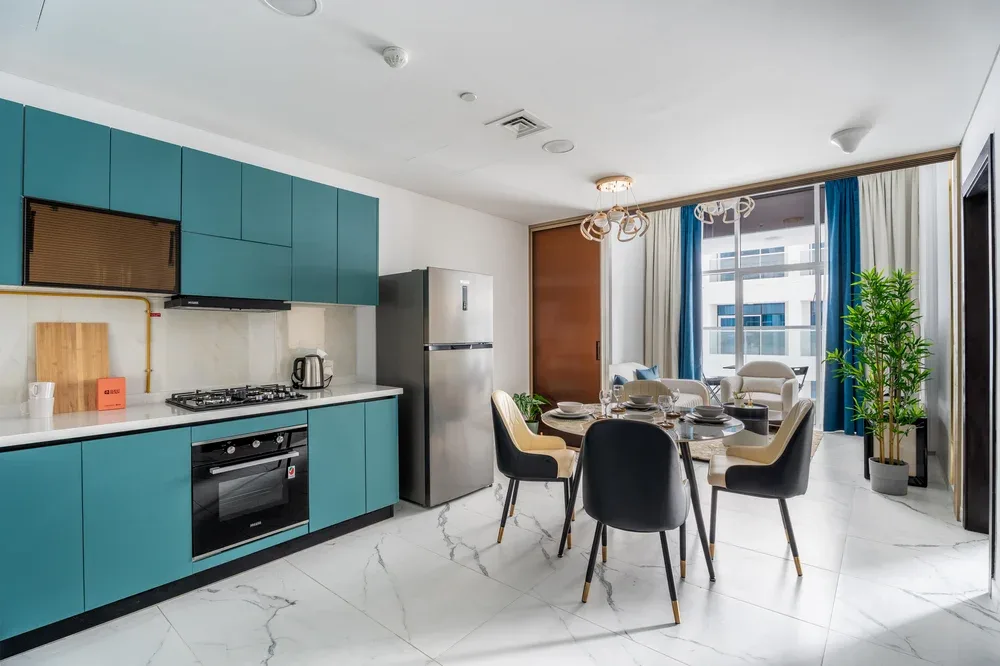 Una cocina y comedor modernos, con gabinetes turquesa y una mesa junto a las ventanas.