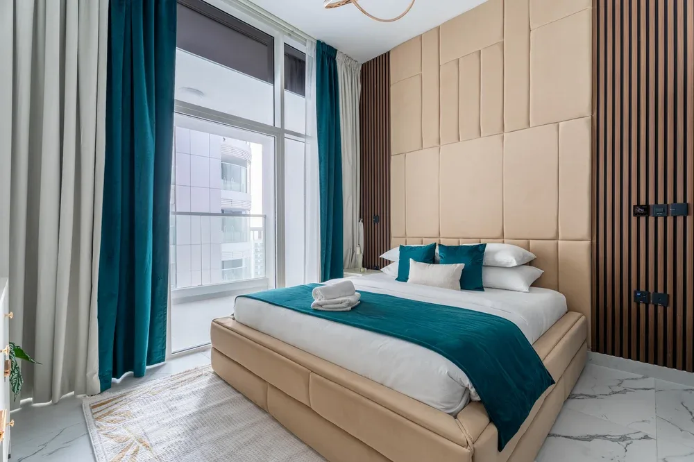 Un dormitorio con una cama vestida de blanco y turquesa junto a una ventana grande.