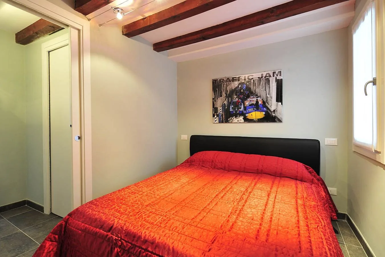 Un dormitorio con una cama cubierta con una colcha roja brillante y un cuadro sobre el cabecero.