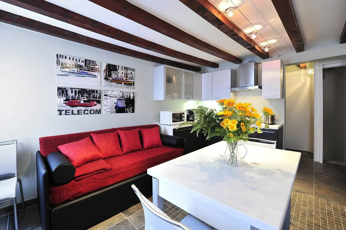 A modern kitchen and dining area has a red sofa and flowers on the table.