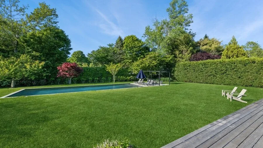A broad lawn stretches beside a swimming pool, with trees lining the garden.