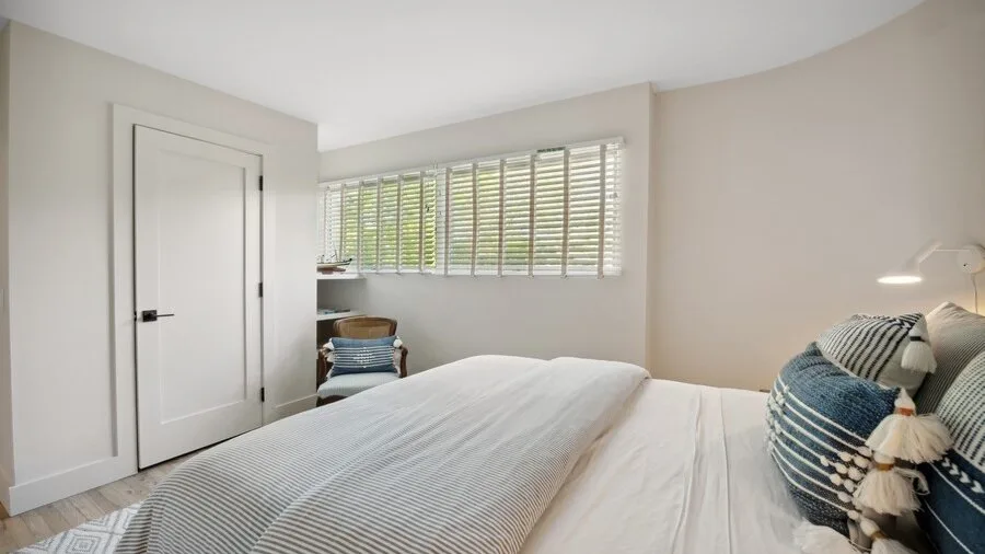 A bright bedroom with a bed, a window, and white blinds.