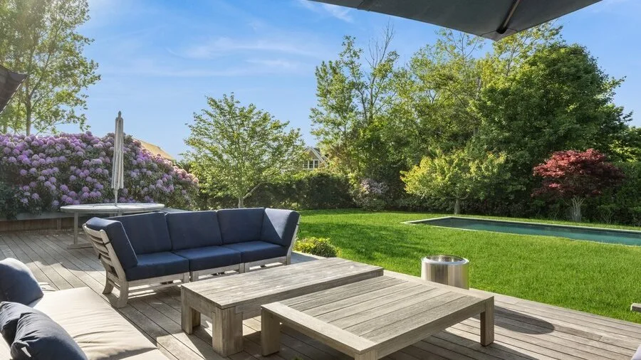 A garden patio has outdoor seating arranged around low wooden tables.