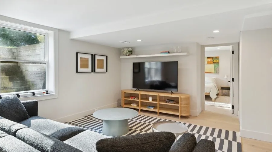 A bright living room with a television, low wooden stand, and seating.