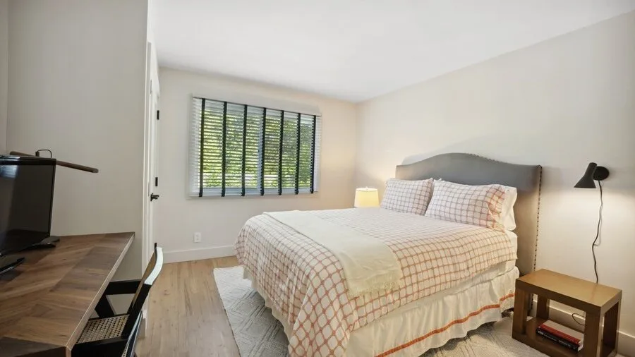 A bright bedroom with a bed, a window, and a desk.