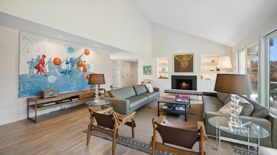 A bright living room with seating arranged around a coffee table and fireplace.