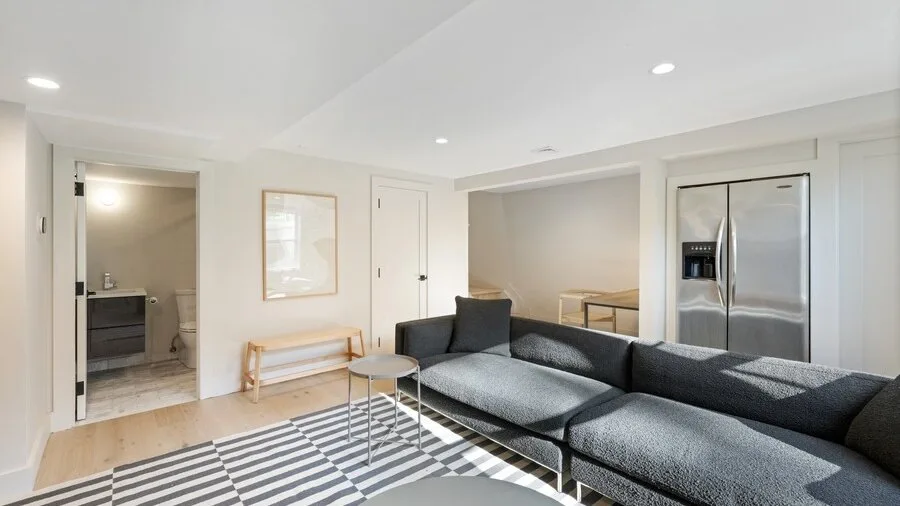 A living room with dark seating, a striped rug, and an open kitchen.