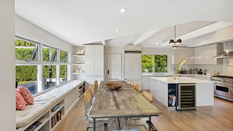 Bright kitchen and dining area with a long table beside large windows.