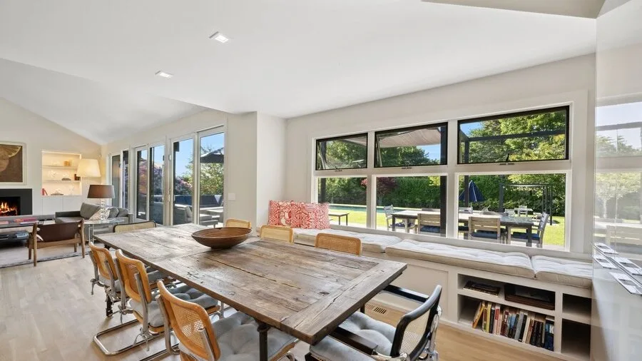 A bright open-plan living and dining area with a large wooden table and garden views.