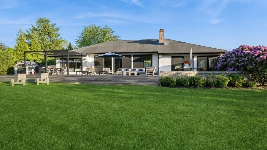 A modern house opens onto a broad lawn and a furnished outdoor terrace.