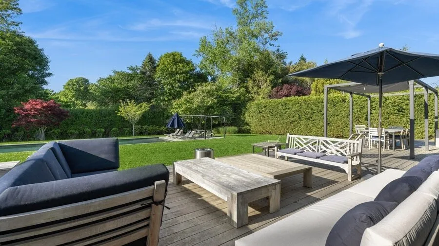 A wooden deck with outdoor seating and a large umbrella overlooks a green garden.