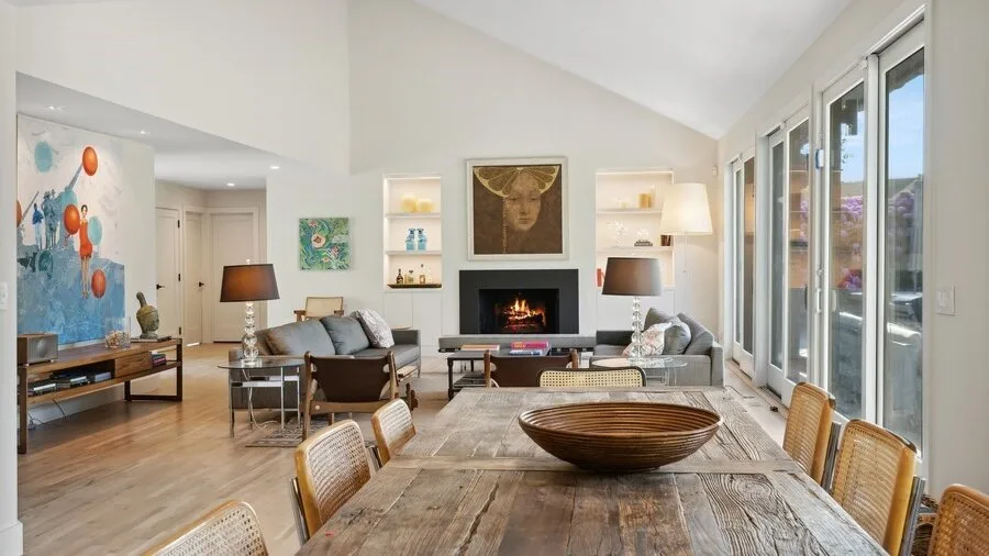 A bright living and dining room with a fireplace and large windows.