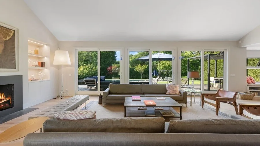 A bright living room with seating arranged around a coffee table and large windows.