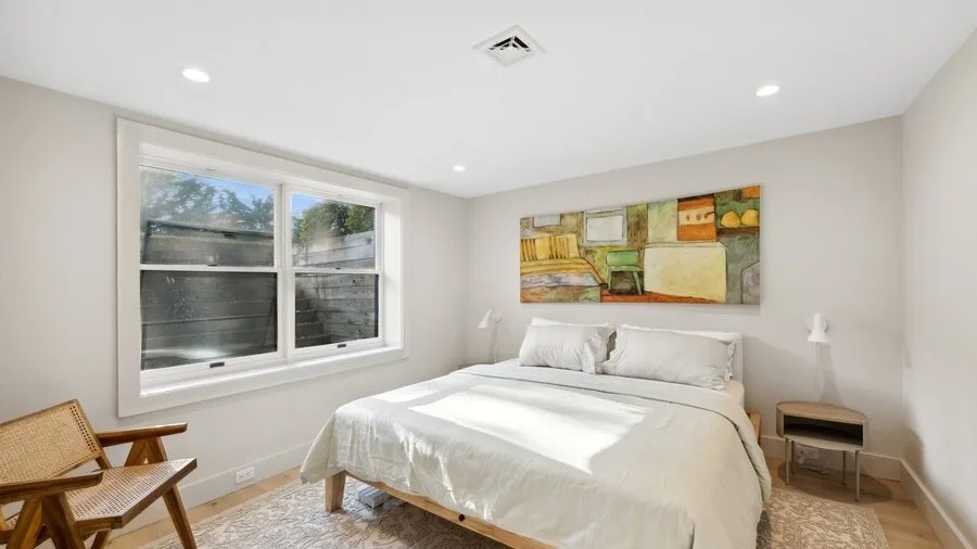 A bright bedroom with a bed beneath a colorful wall painting.