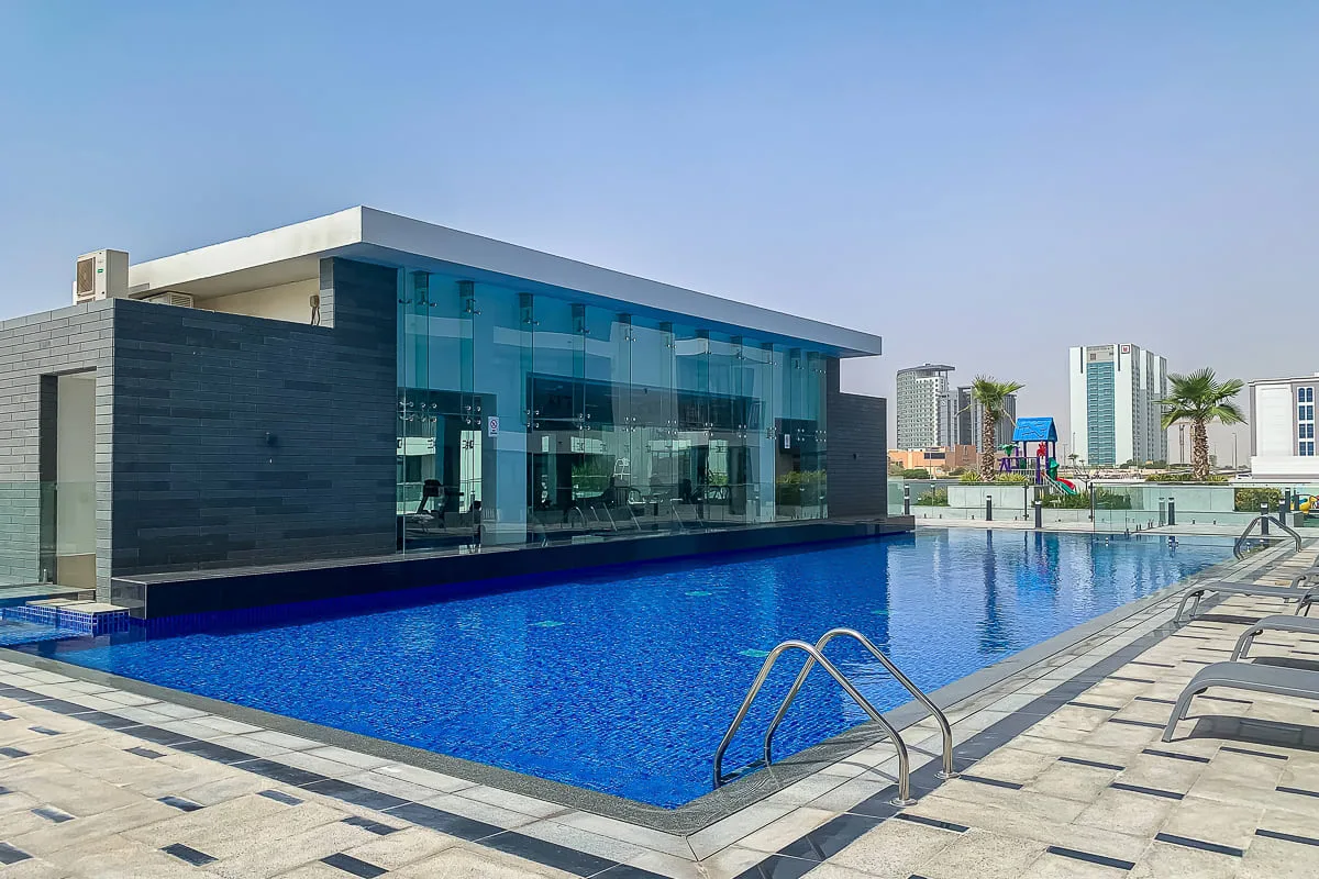 Un edificio moderno con fachada de vidrio da a una piscina y su zona de descanso.