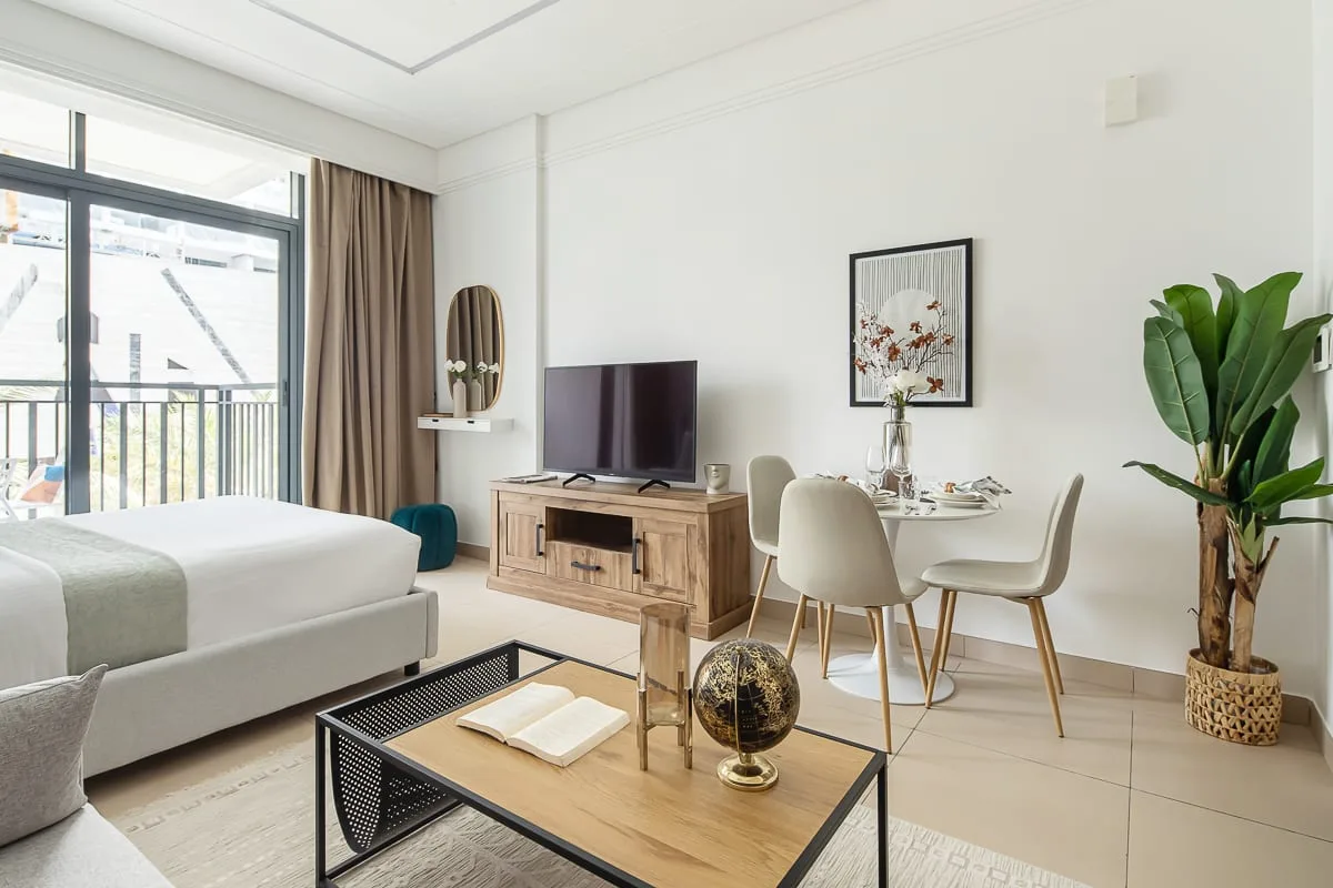 Un dormitorio luminoso con zona de comedor, cama, televisor y mesa.