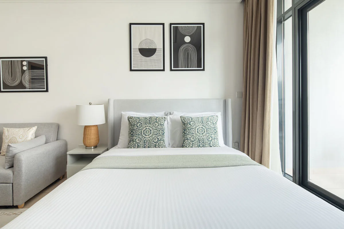 Un dormitorio luminoso con una cama tendida y grandes ventanas.