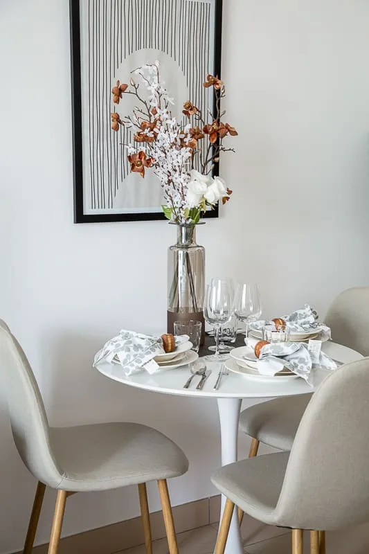 Un rincón de comedor con la mesa puesta y un jarrón de flores bajo un cuadro.